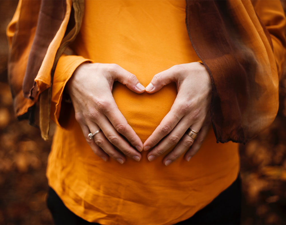 woman holding hands over stomach in a heart symbol